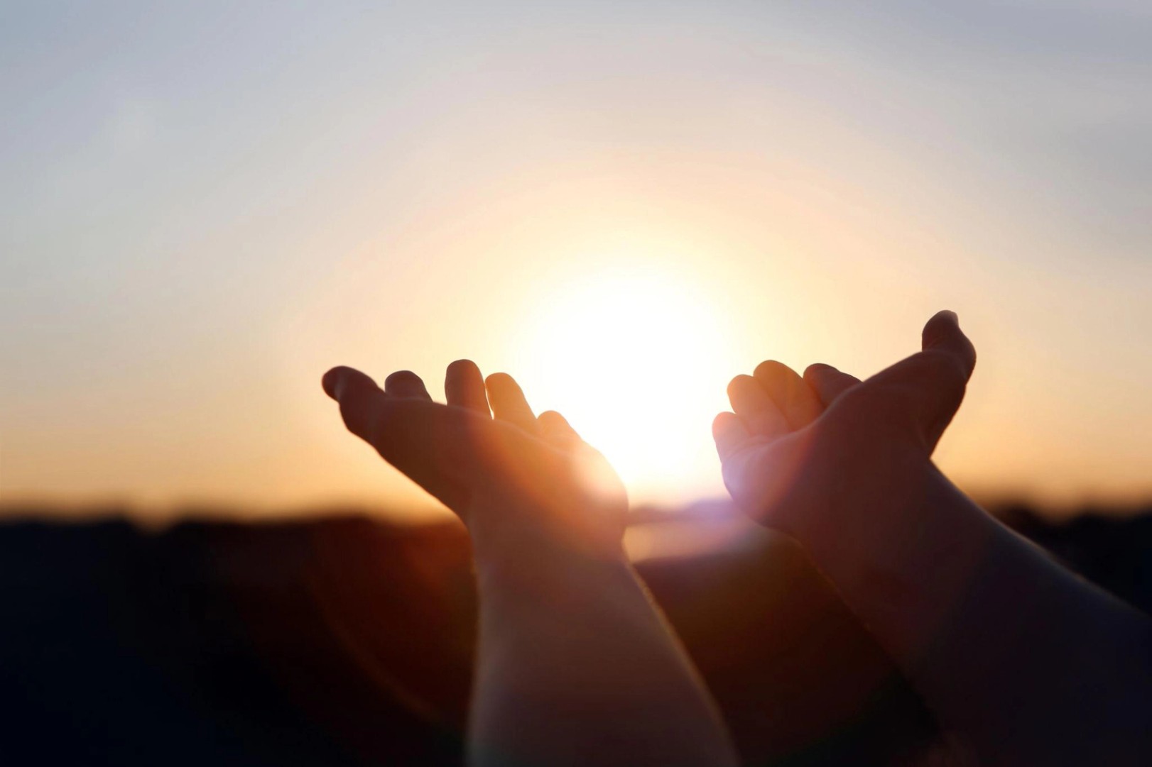 New Year's sunrise, brilliant light and rays of light shining through hands stretched out toward the rising sun, concept of hope and wishes for the future