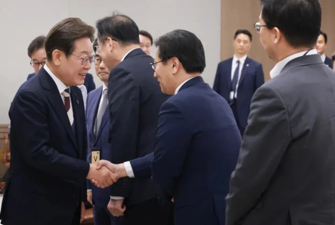 이재명 민생회복지원금 - 정장 차림의 정치인과 관계자들이 회의실에서 악수하며 인사하는 모습