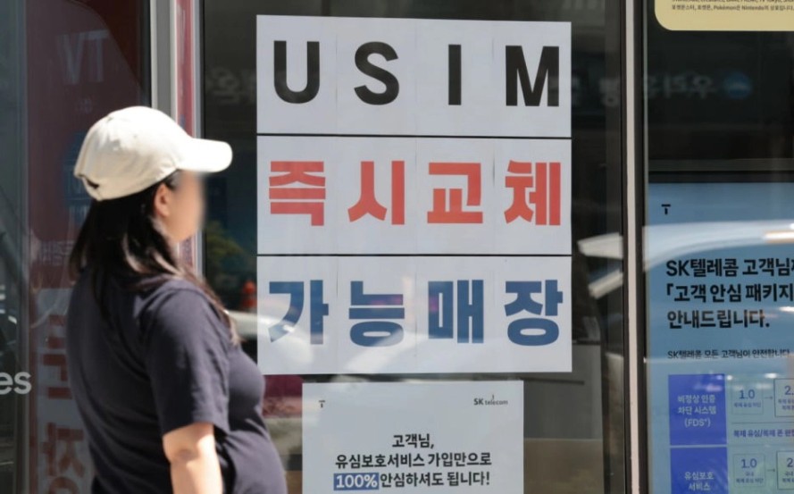 SK텔레콤 매장 유리창에 부착된 "USIM 즉시교체 가능매장" 안내문을 바라보는 여성