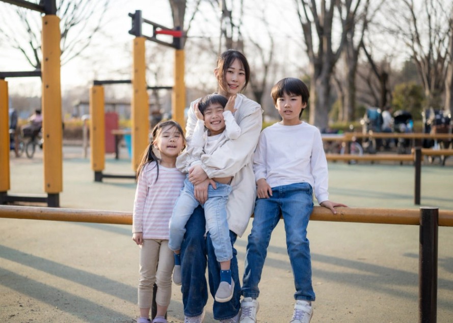 놀이터에서 자녀 셋과 함께 앉아 환하게 웃고 있는 엄마