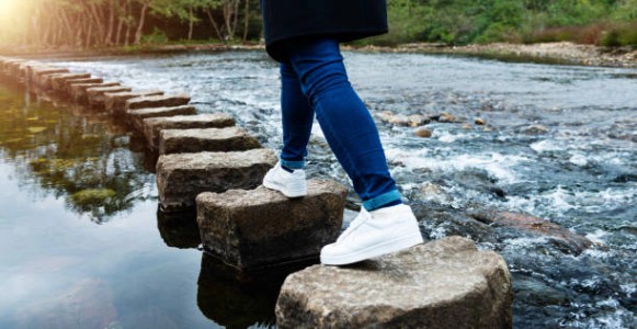 woman crossing stepping stones on a river - 다리 뉴스 사진 이미지